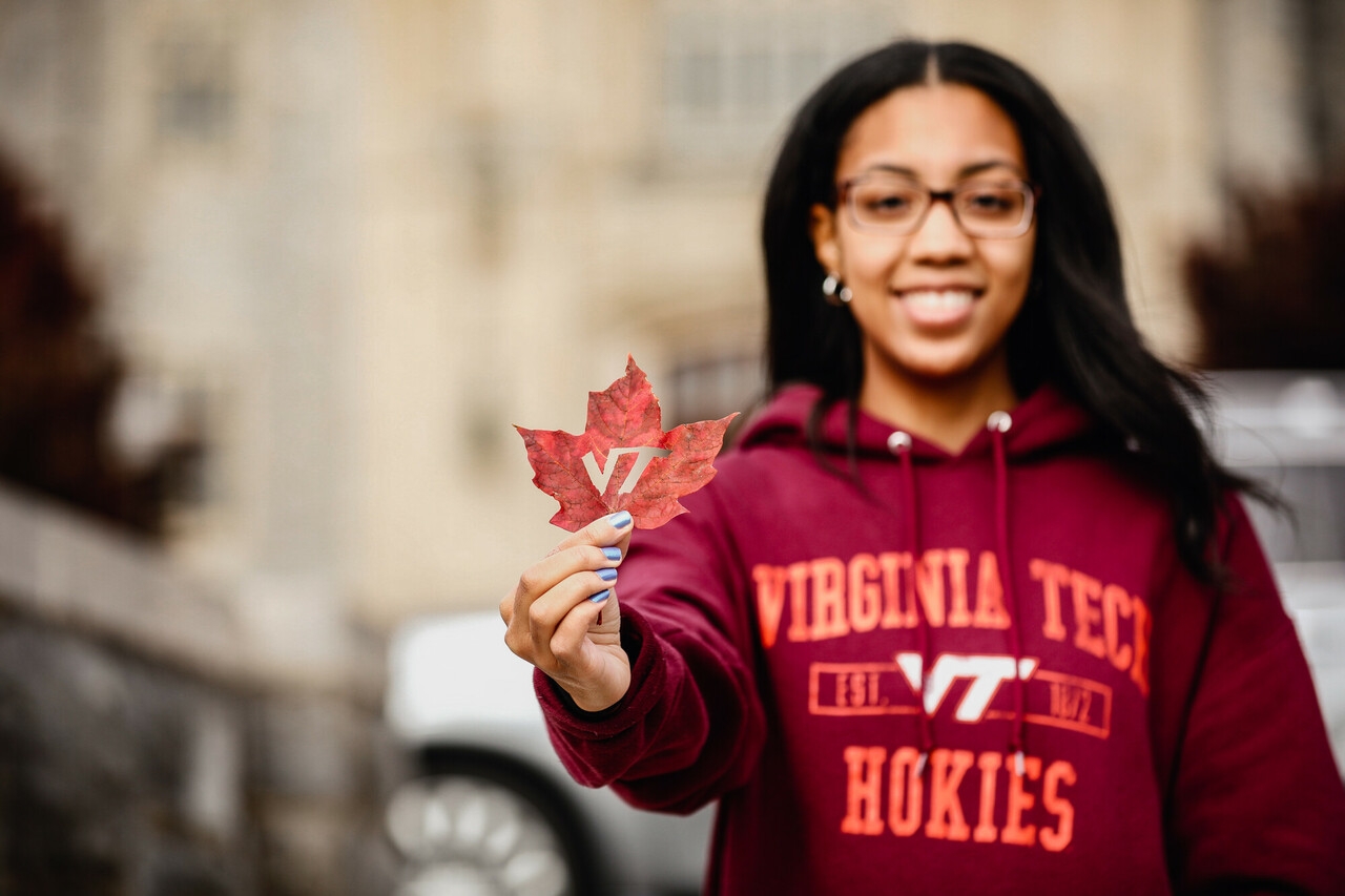 Student holding a leaf with the Virginia Tech athletic logo cut out of the center.